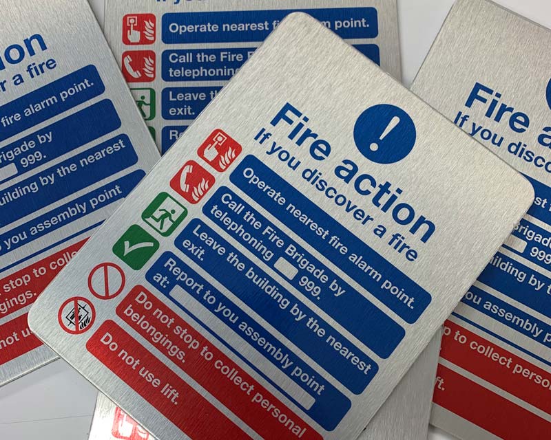 A printed fire action sign on brushed aluminium composite panel A printed fire action sign on brushed aluminium composite panel